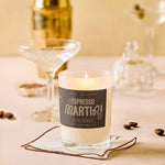 Candle labeled 'Espresso Martini' on a table with coffee beans and glasses in the background