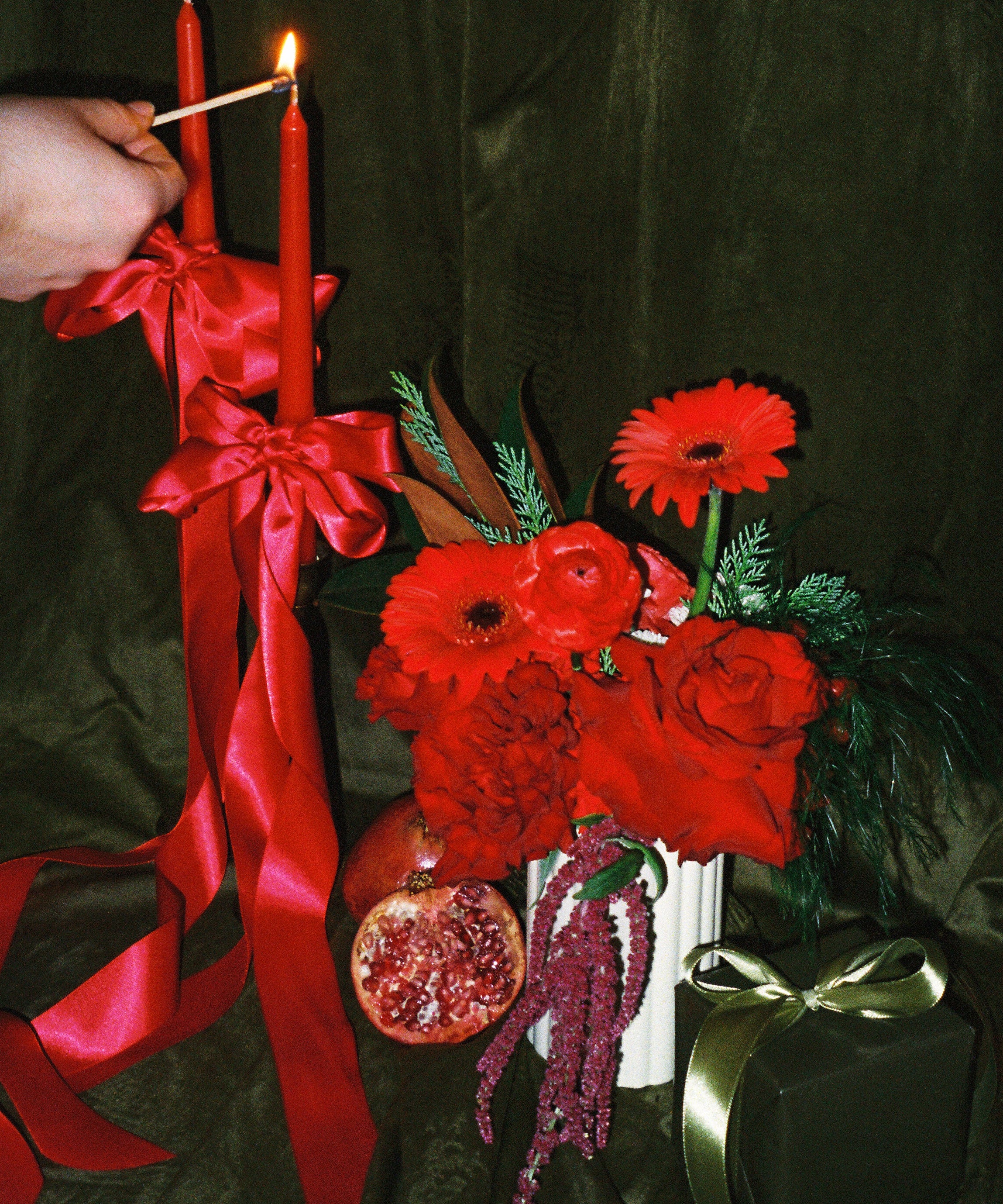 A floral arrangement featuring primarily red flowers and green foliage, with a person lighting a candle on top. The arrangement is placed in a vase, which is not visible, and there is a card with '11/9/13' printed at the top.