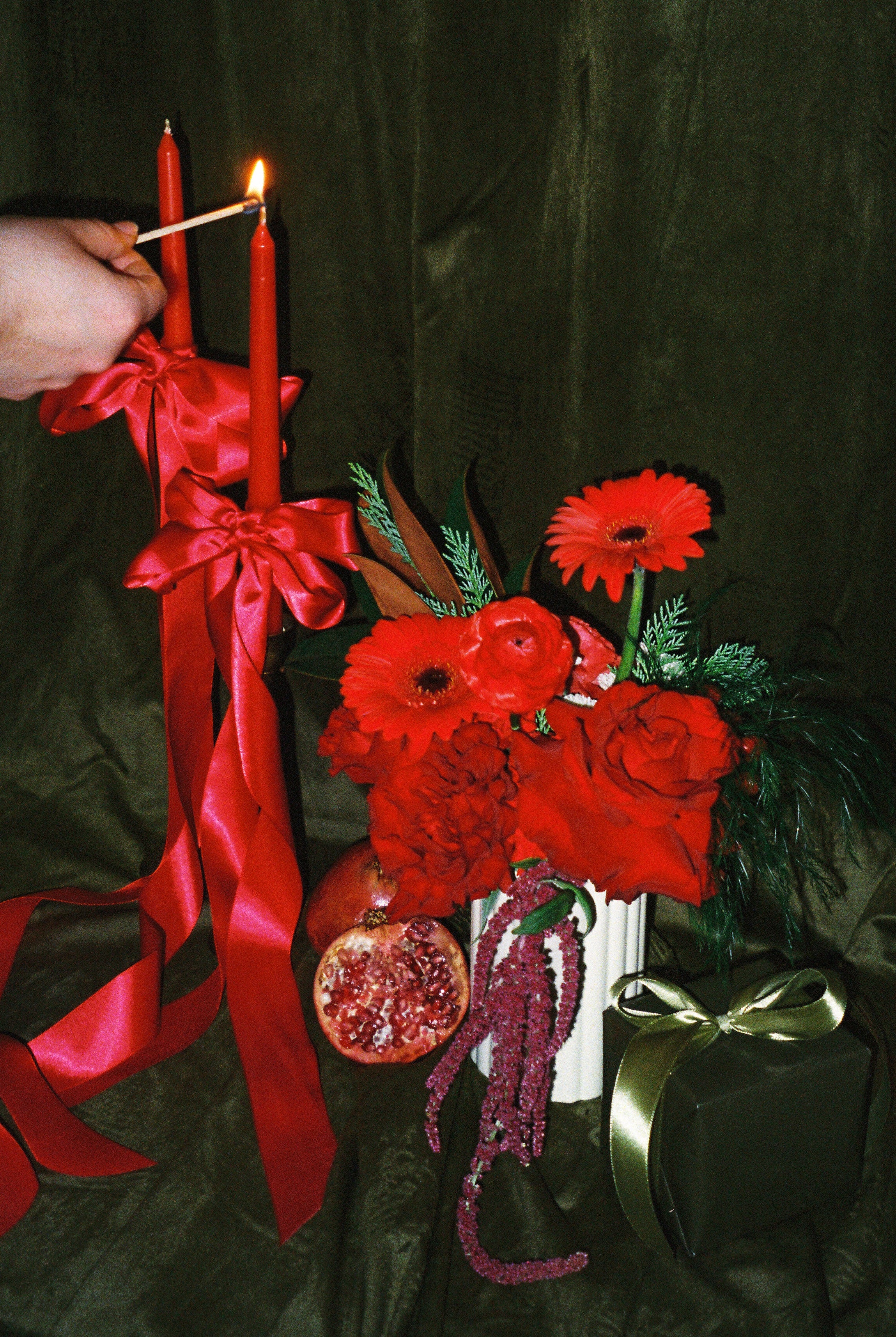 A floral arrangement featuring primarily red flowers and green foliage, with a person lighting a candle on top. The arrangement is placed in a vase, which is not visible, and there is a card with '11/9/13' printed at the top.